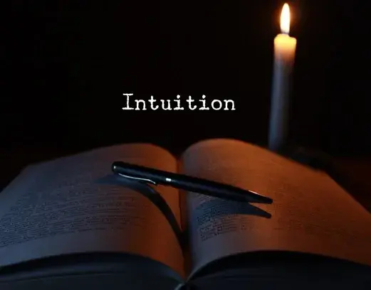 black background with a white candle, an open book with a pen on it and text "intuition"