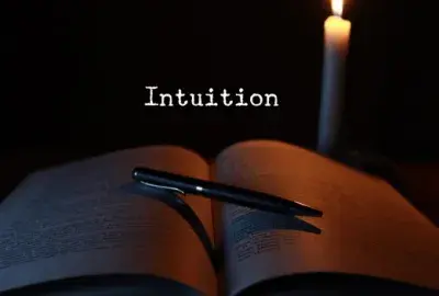 black background with a white candle, an open book with a pen on it and text "intuition"