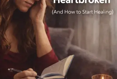 What to do when heartbroken image showing woman journaling with tarot cards and candle representing emotional healing and relationship recovery